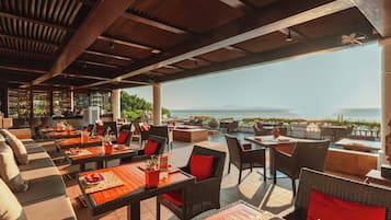 An outdoor seating area with tables and chairs, a pool, and a view of the sea.