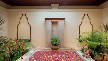 A serene indoor space with a central water feature, surrounded by lush greenery and a decorative archway.