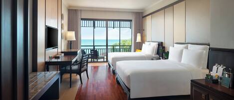 A hotel room with a large window, a desk, two beds, and a TV.