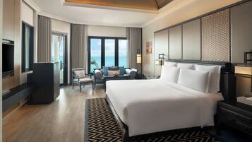 A hotel room with a large bed, a desk, a chair, a television, and a view of the ocean.