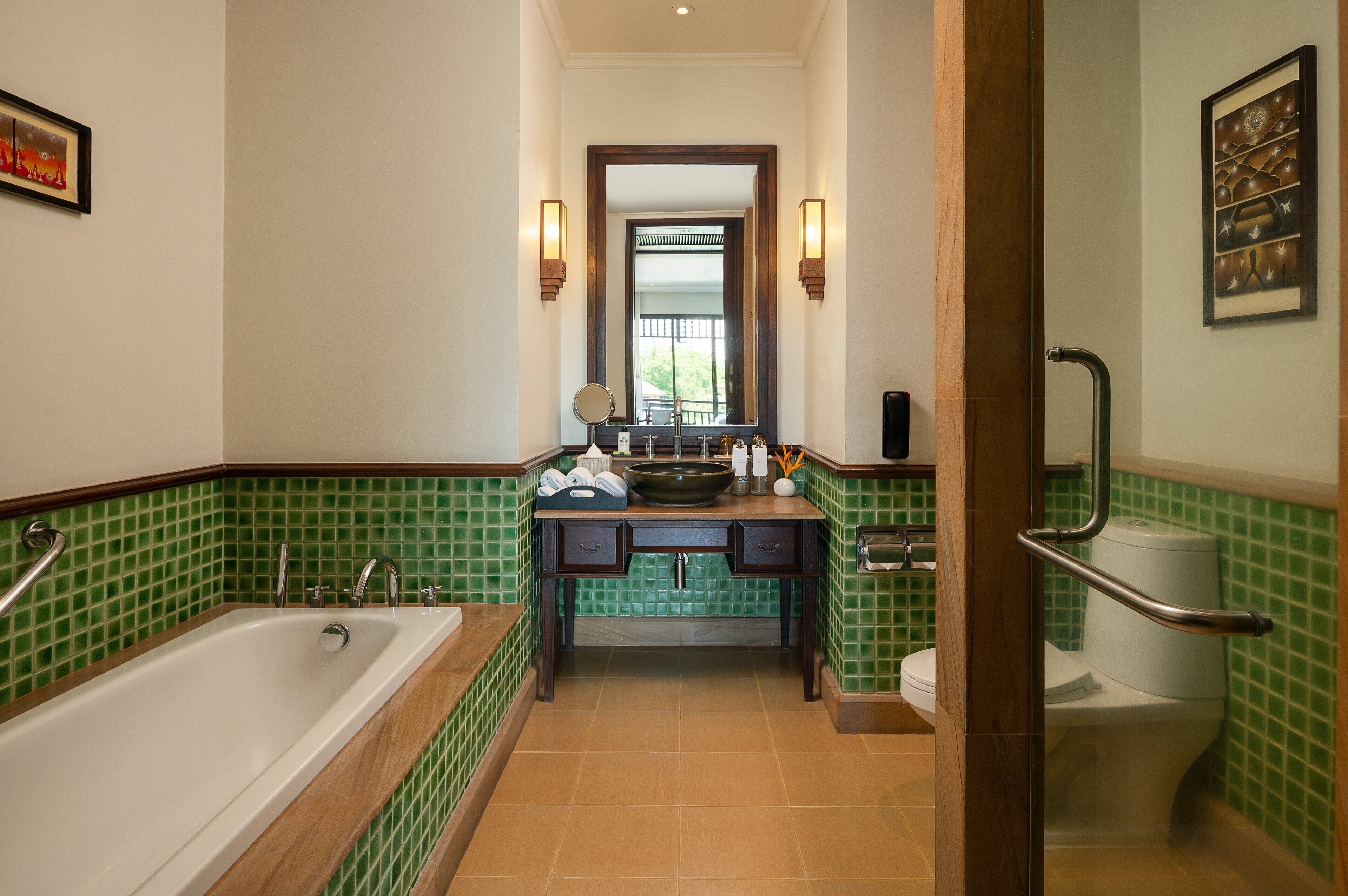 Ein Badezimmer mit Badewanne, Waschbecken und Toilette, mit grünen Fliesenwänden und Holzelementen.