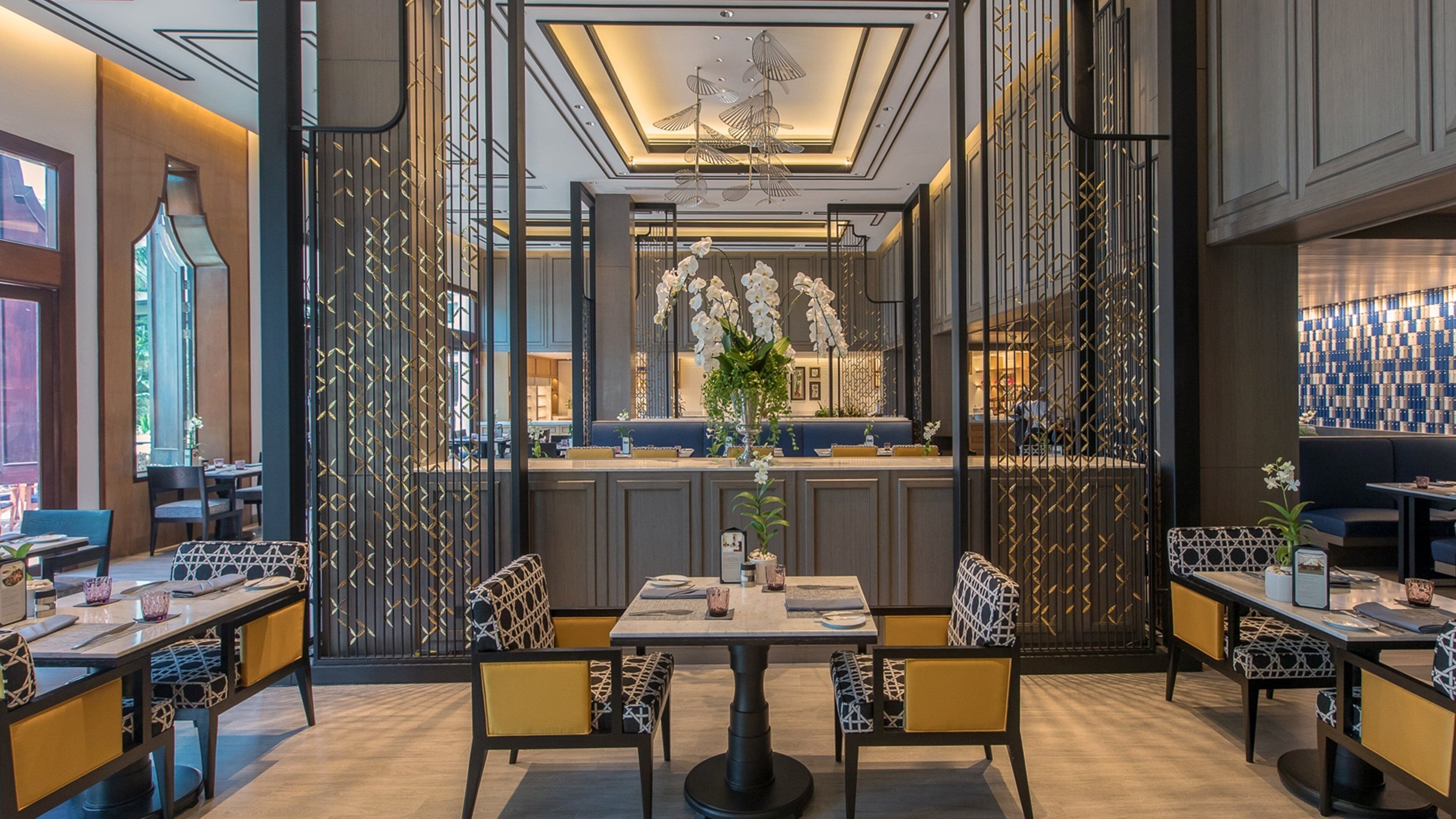 Un intérieur de restaurant moderne avec une table à manger centrale, des banquettes et un mur orné de motifs.