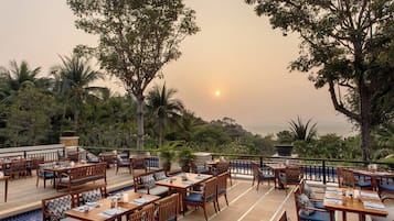 Un espace de restauration en plein air, avec des tables et des chaises en bois, entouré d’une végétation luxuriante et offrant une vue panoramique.