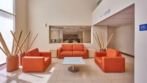 Un vestíbulo moderno con sofás naranja, una mesa central y plantas de bambú.