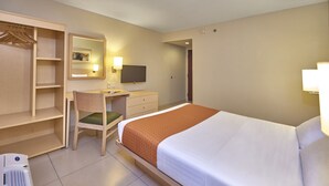 Habitación de hotel con cama, escritorio, silla, armario, espejo y televisión.