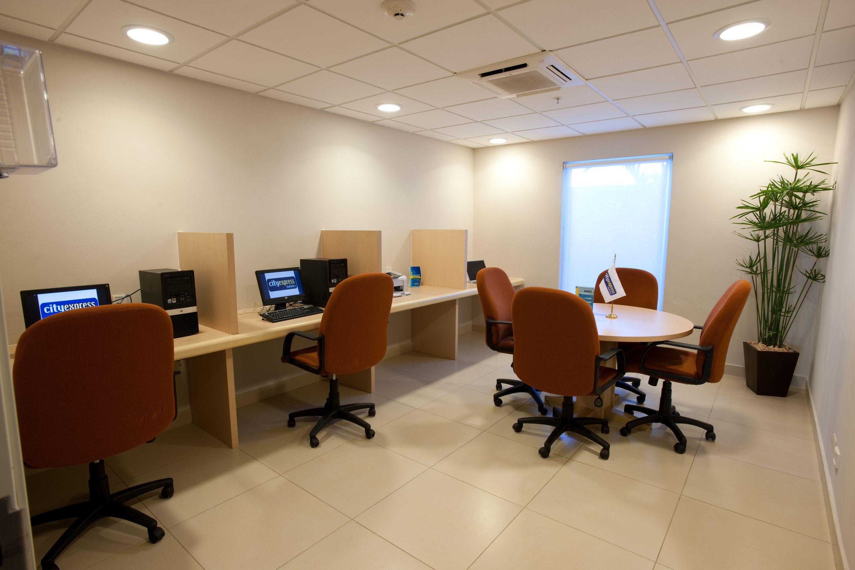 Un espacio de oficina moderno con cubículos, sillas de oficina color naranja y computadoras.