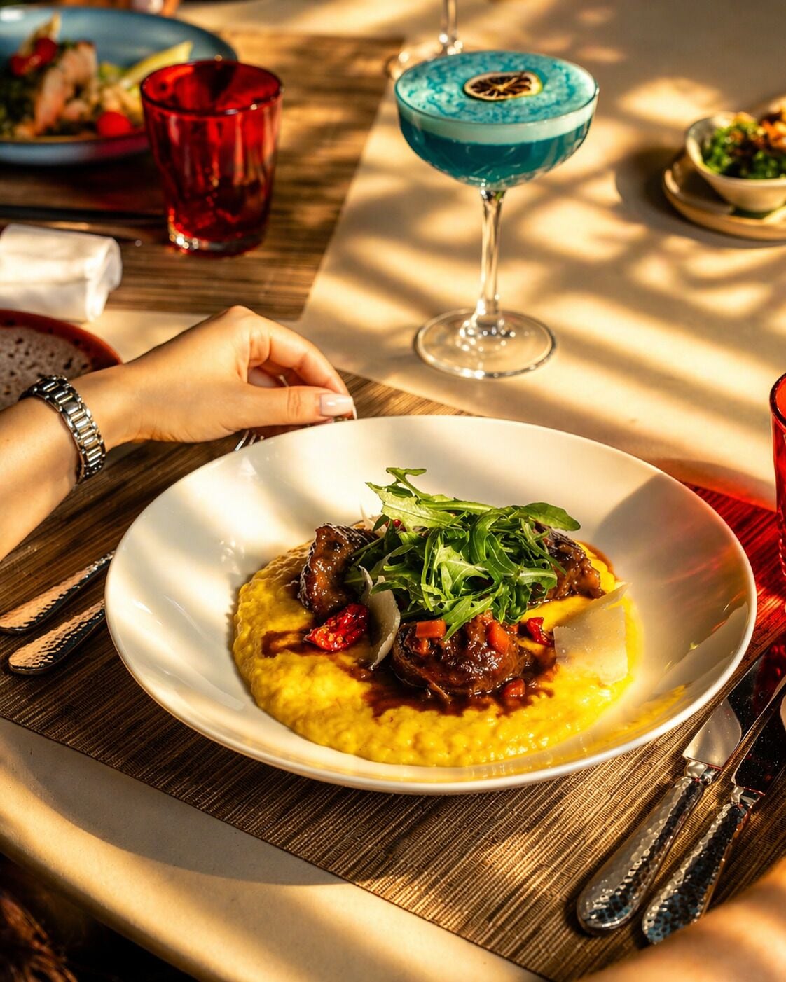 Una mesa de comedor con un plato de comida, una copa de cóctel azul y un vaso rojo.