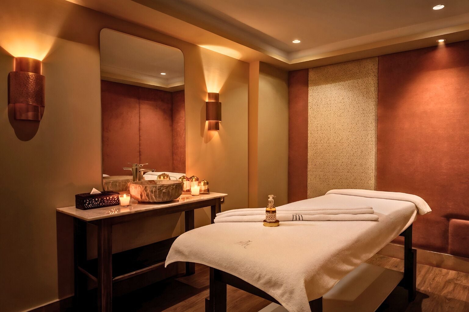 Sala de spa com mesa de massagem, pia com cuba grande, velas e espelho.