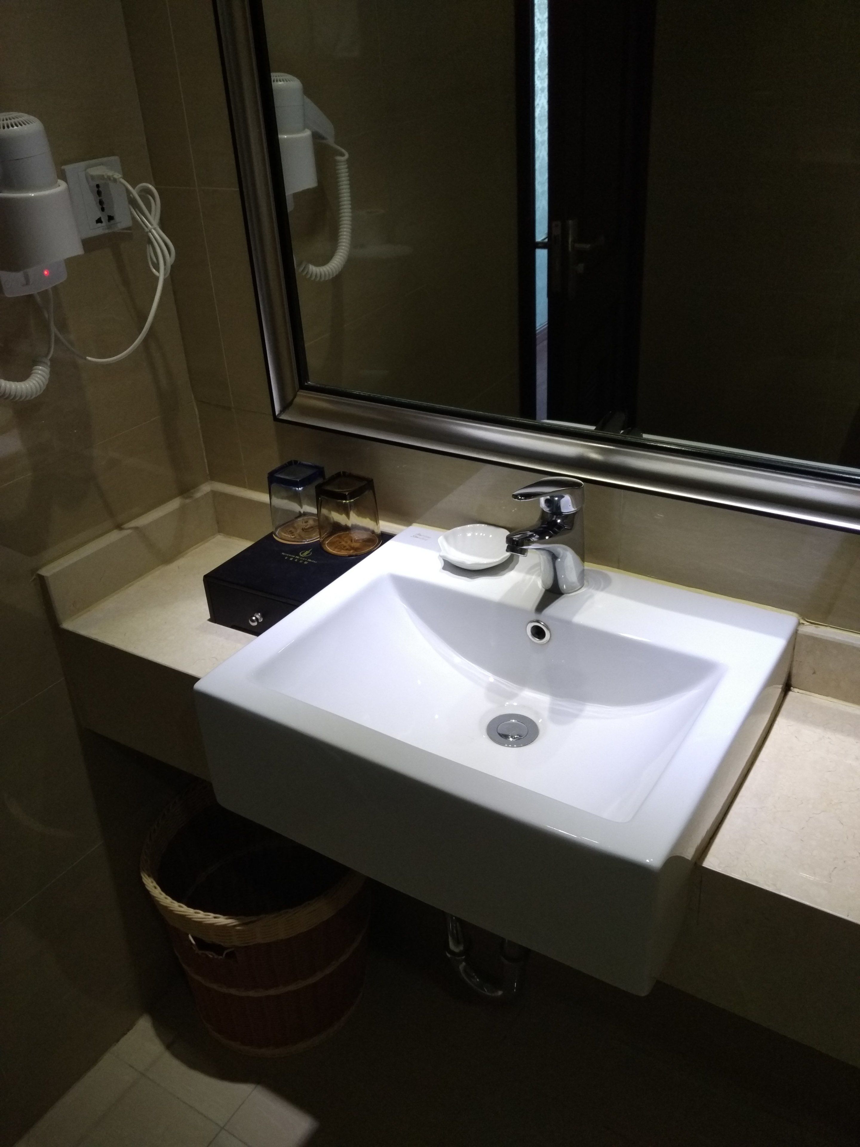 A bathroom with a white sink, a mirror, and a hairdryer on the wall.