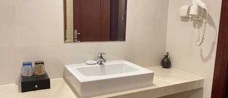 A bathroom with a white sink, a mirror, a hairdryer, and a vase on the counter.