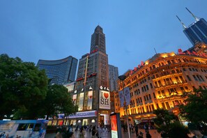 A cityscape with a prominent building featuring a large 'I ♥ SH' sign, surrounded by other illuminated buildings and a clear sky.
