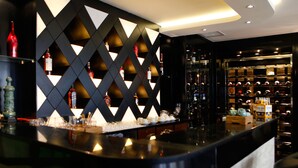 A bar area with a black diamond-patterned wall, shelves with bottles, and a counter with glasses and bottles. - Seventh Heaven Hotel (Shanghai)