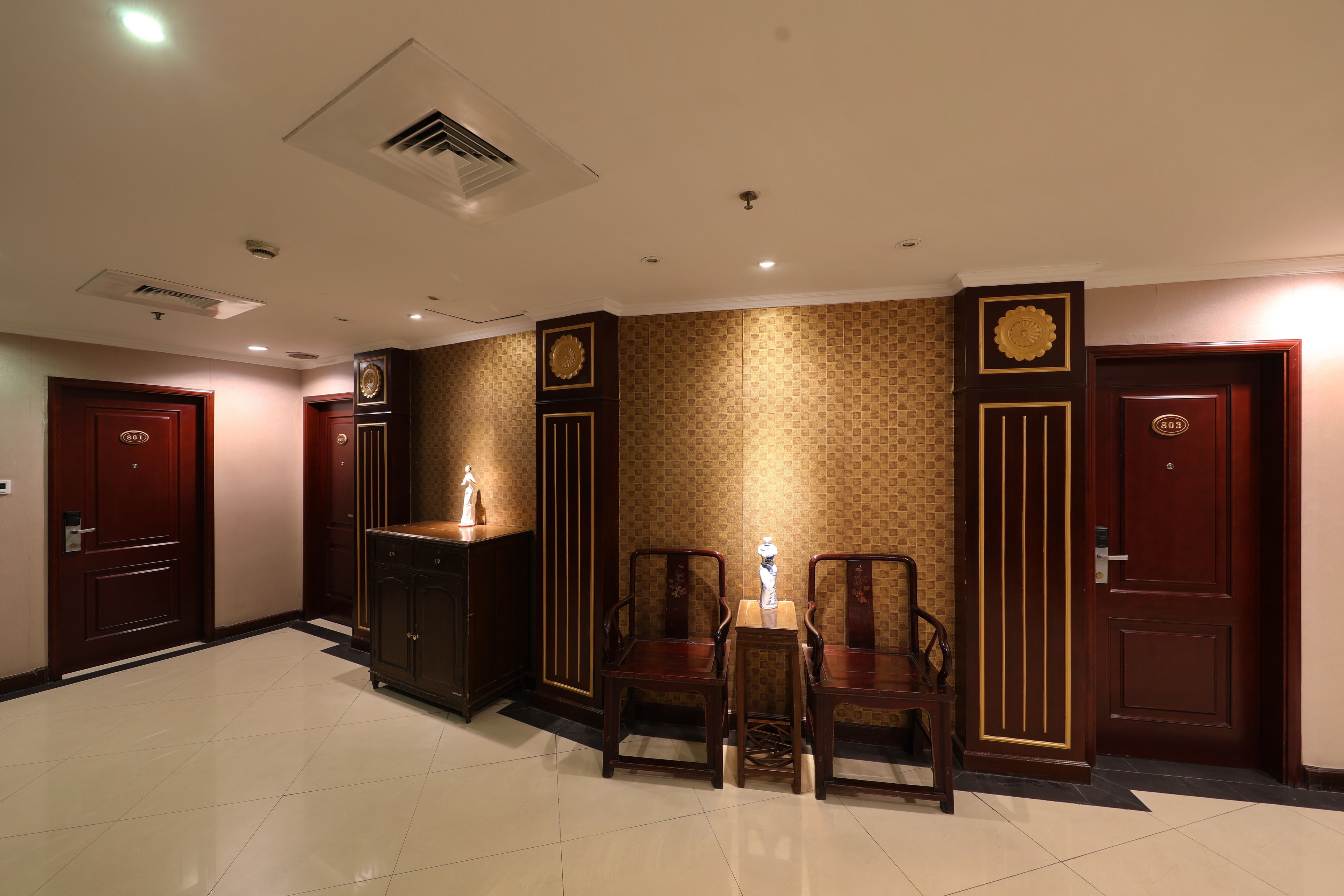 A hotel lobby with a reception desk, two wooden chairs, a small table, and three doors.