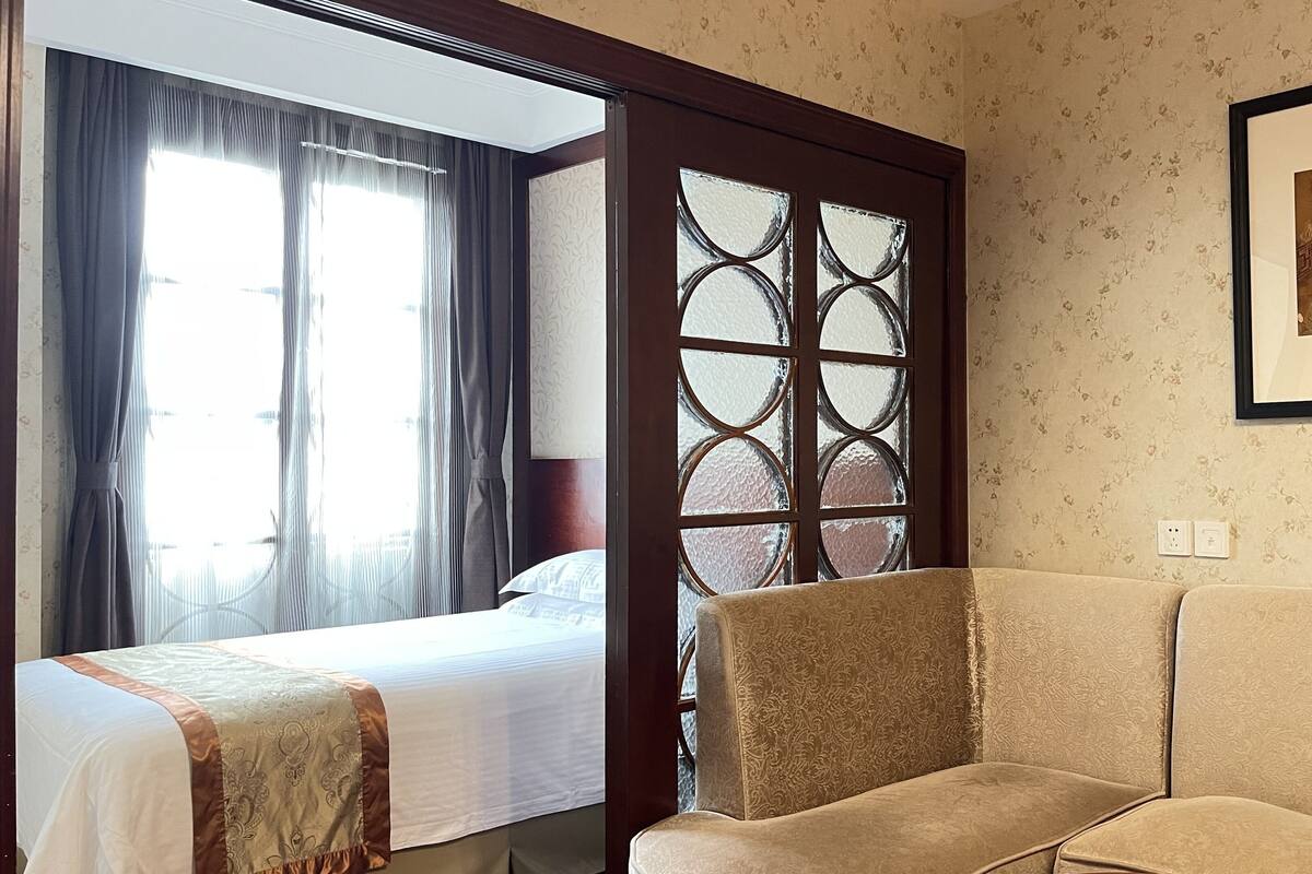 A hotel room with a bed, a sofa, a decorative glass partition, and a framed picture on the wall.