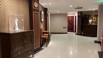 Un vestíbulo de hotel con un mostrador de recepción de madera, una vitrina transparente y un suelo de baldosas.