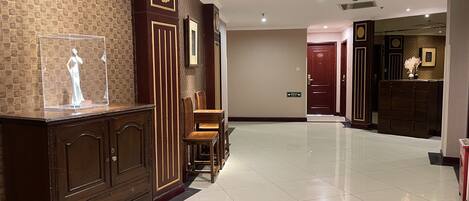 Un vestíbulo de hotel con un mostrador de recepción de madera, una vitrina transparente y un suelo de baldosas.