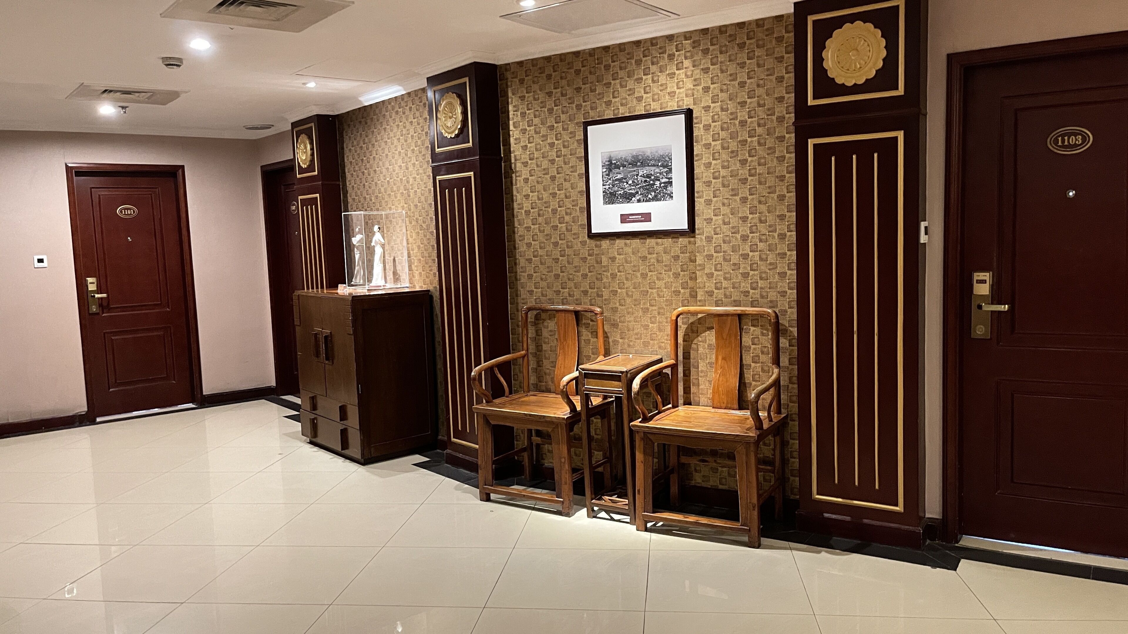 A hotel lobby with a tiled floor, wooden furniture, and a framed picture on the wall.
