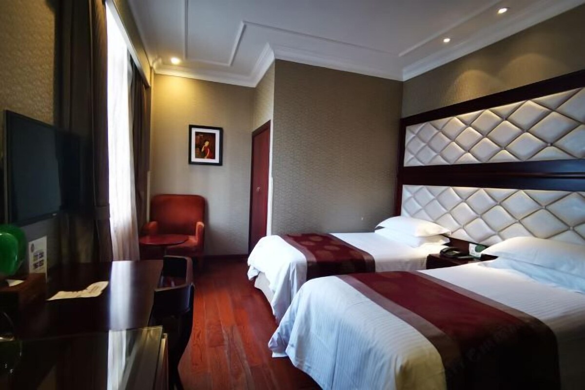 A hotel room with two beds, a desk, a chair, and a television.