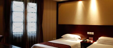 Habitación de hotel con dos camas, un ventanal con cortinas, un escritorio y una mesita de noche con teléfono.