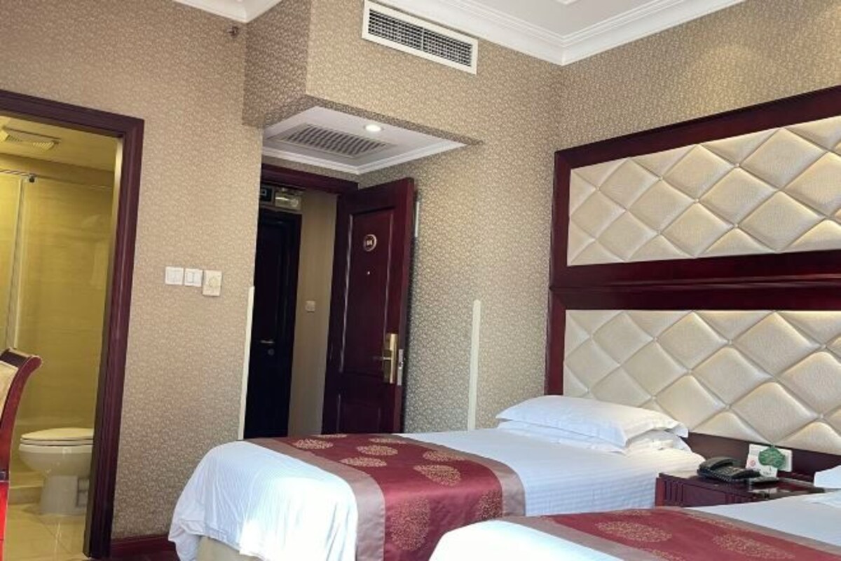 Habitación de hotel con dos camas, cabecera de madera, mesita de noche y puerta que da a otra habitación.