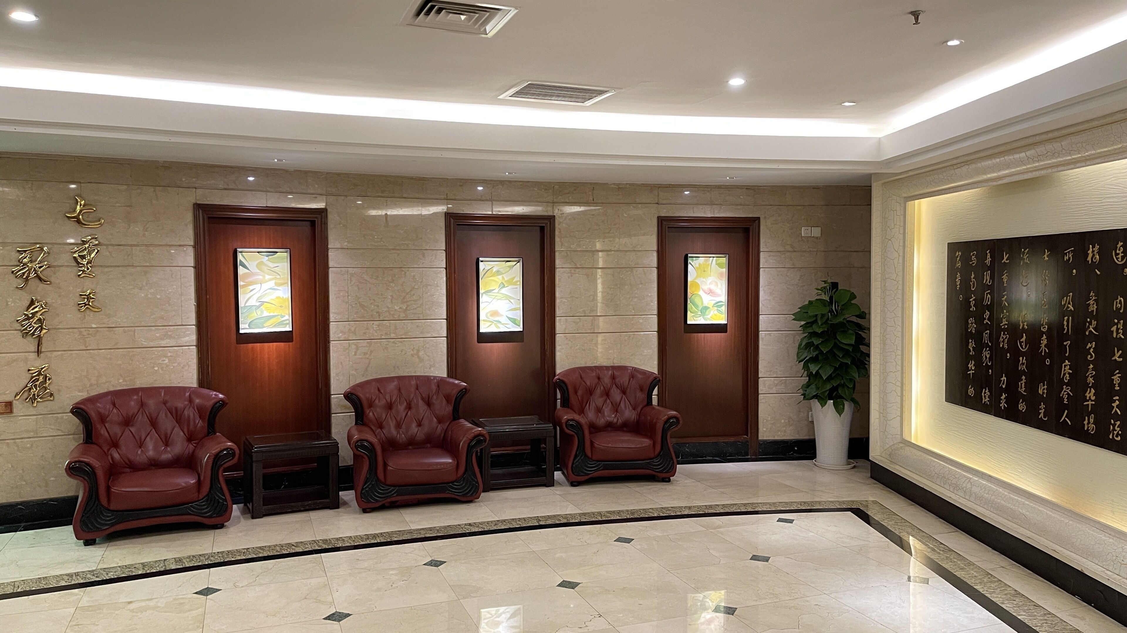 A lobby with three leather armchairs, a potted plant, and a wall with calligraphy.