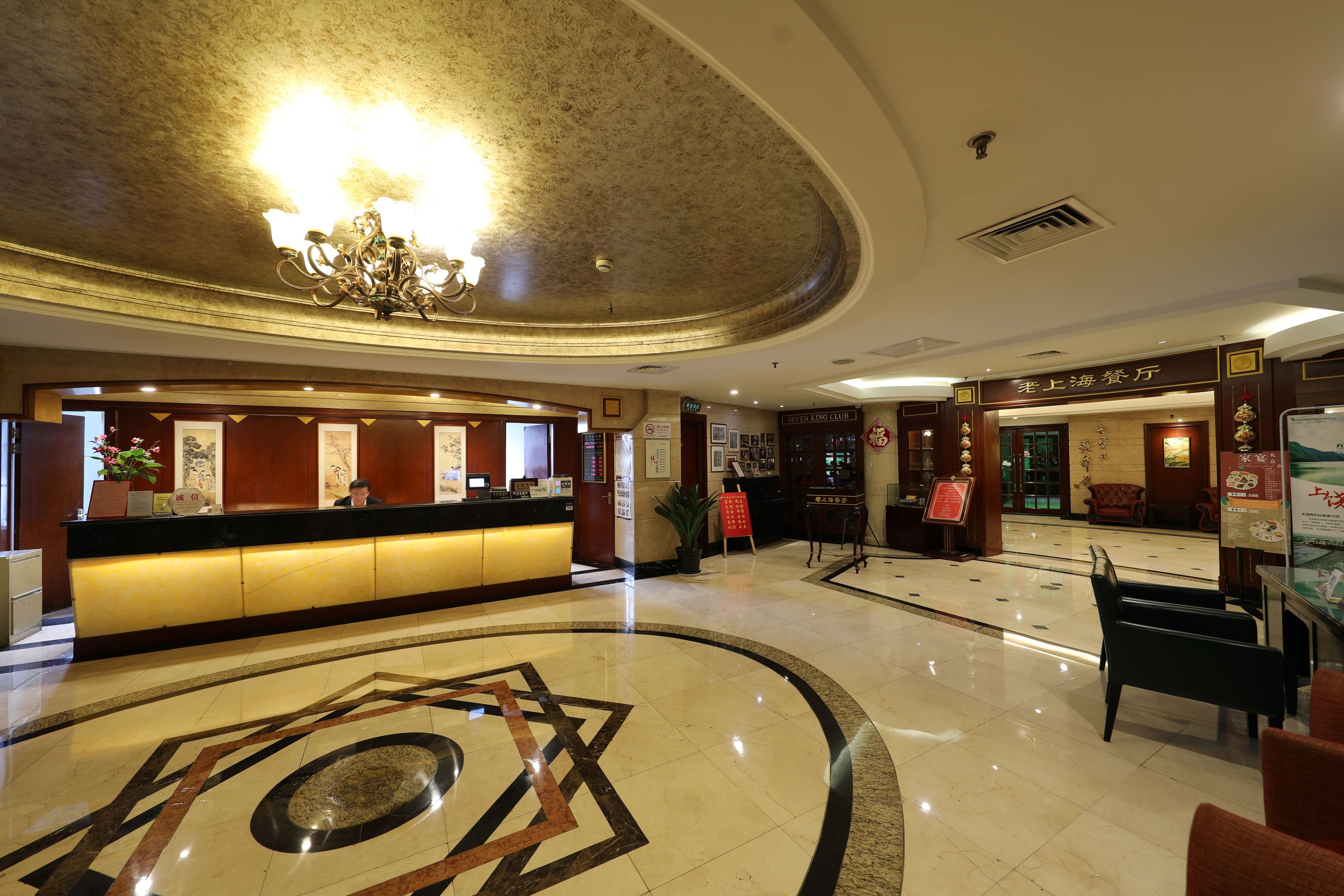 A hotel lobby with a reception desk, a chandelier, and a decorative floor pattern.