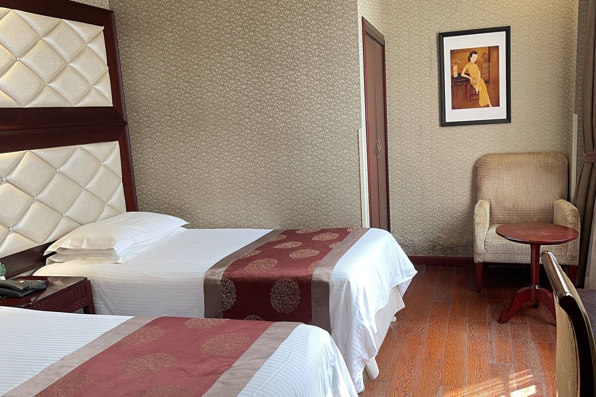 A hotel room with two beds, a chair, a small table, and a framed picture on the wall.