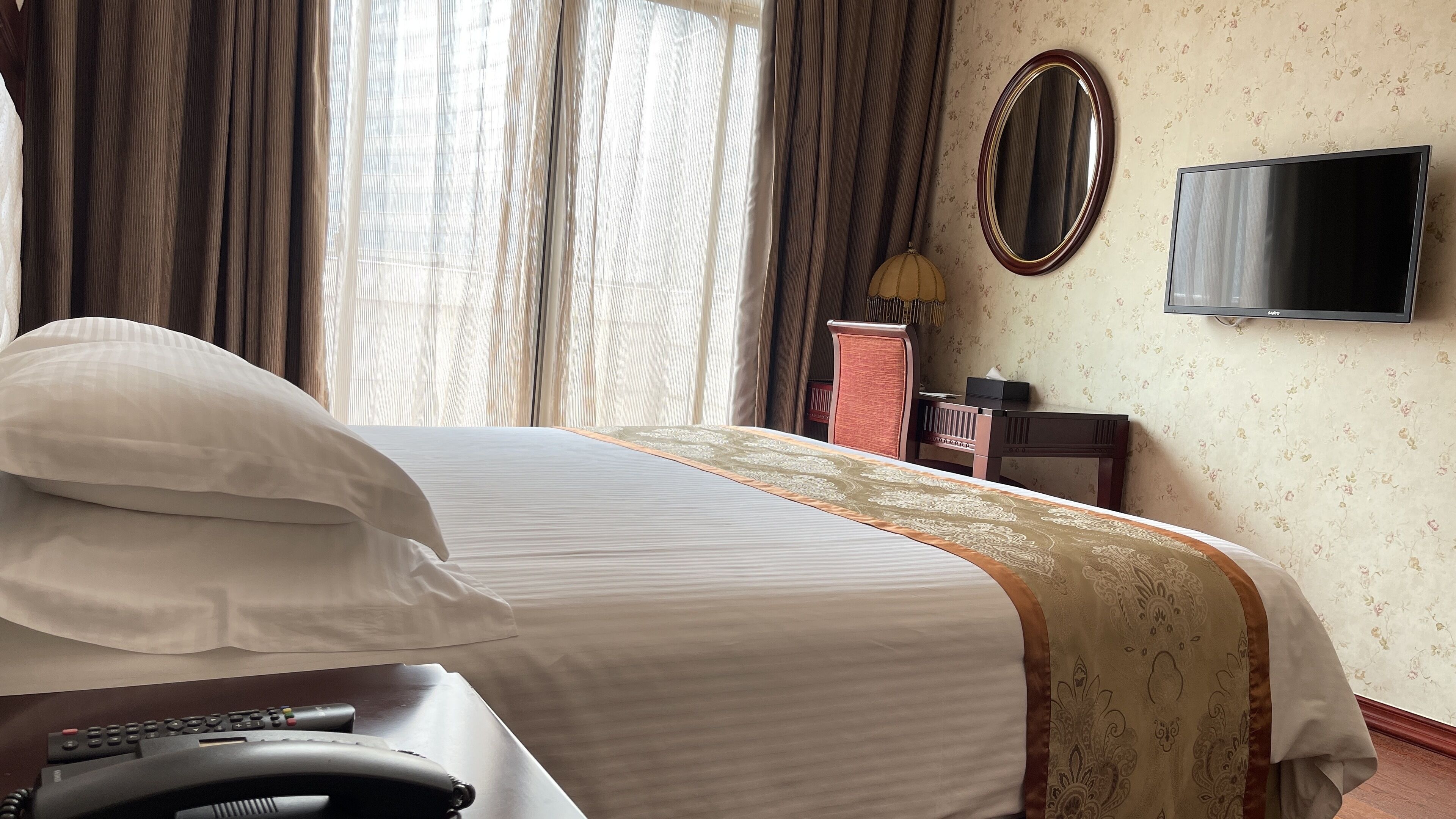 A hotel room with a bed, a desk with a telephone, a television, and a mirror on the wall.