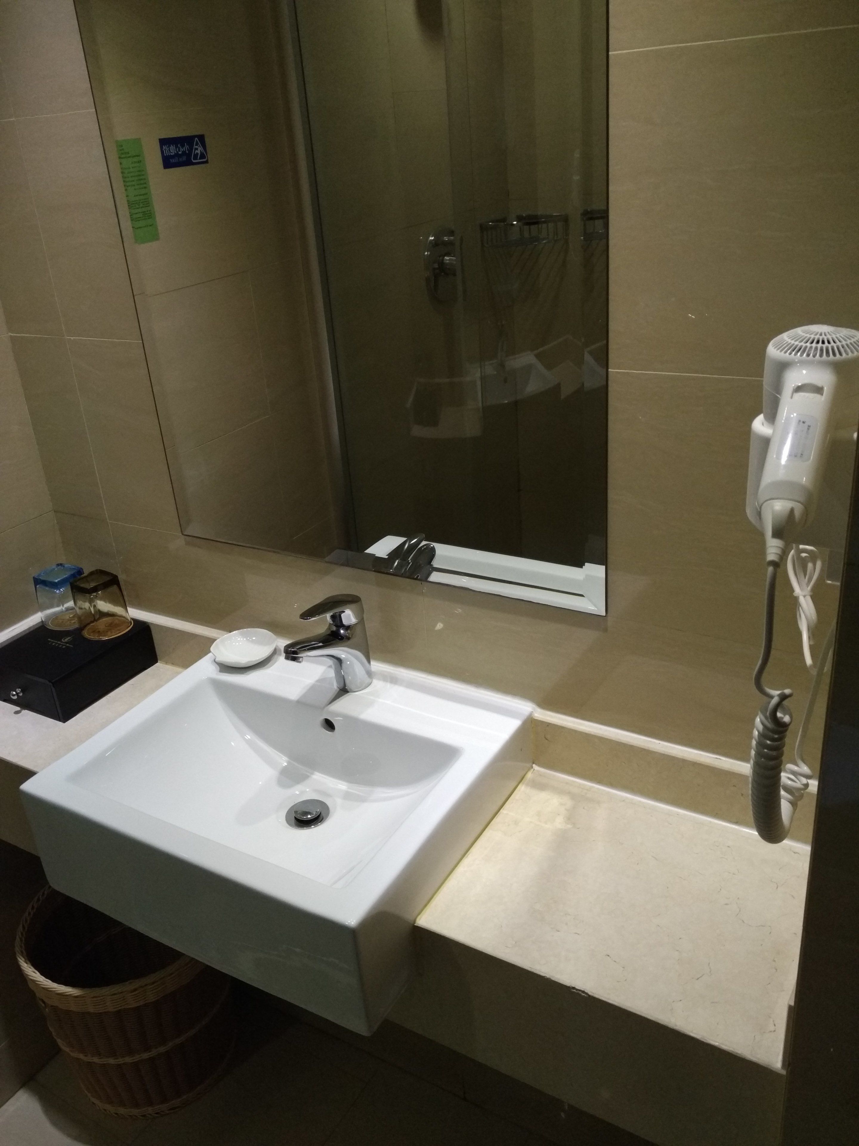 A bathroom with a white sink, a mirror, and a hairdryer on a wall-mounted stand.
