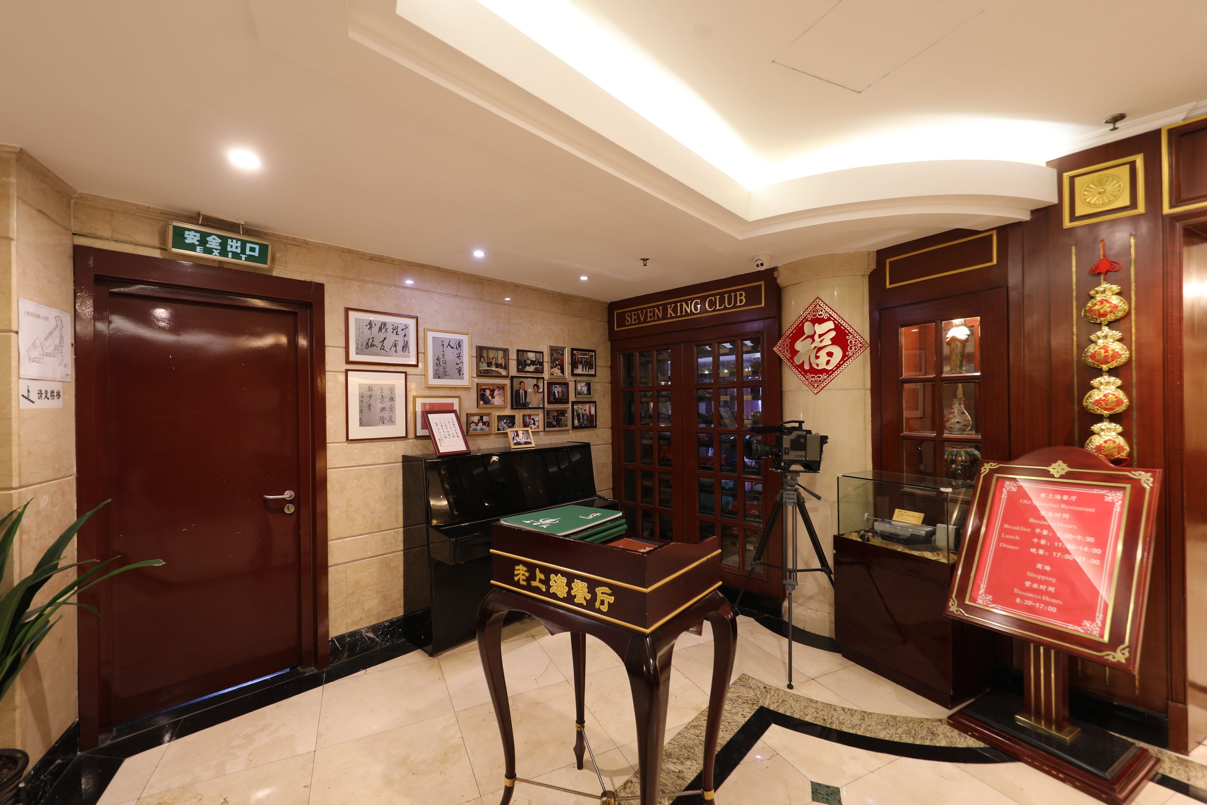 A lobby with a wooden reception desk, framed pictures on the wall, a piano, and a sign for the Seven King Club.