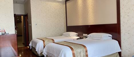A hotel room with two beds, wooden flooring, a large mirror, and a wooden headboard.