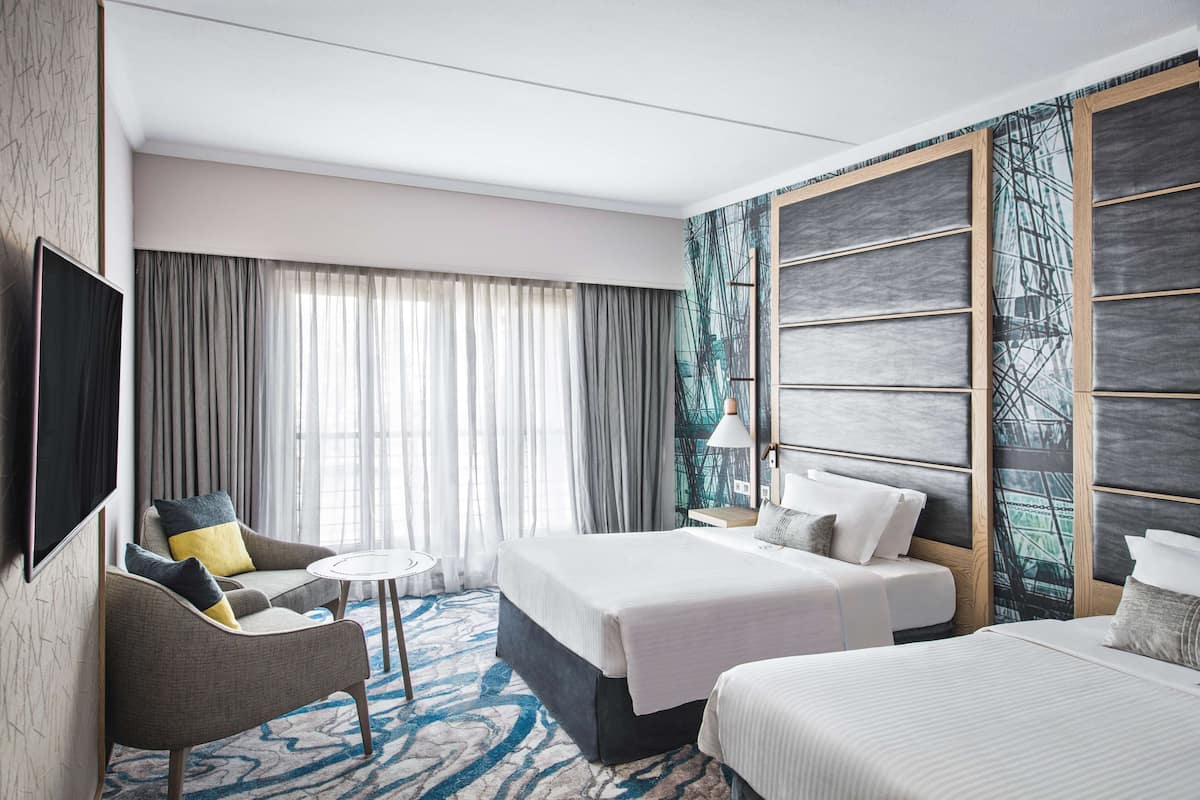 Habitación de hotel con una cama grande, una cama más pequeña, un sofá, un televisor y un ventanal con cortinas.