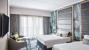 A hotel room with a large bed, a smaller bed, a sofa, a TV, and a large window with curtains.