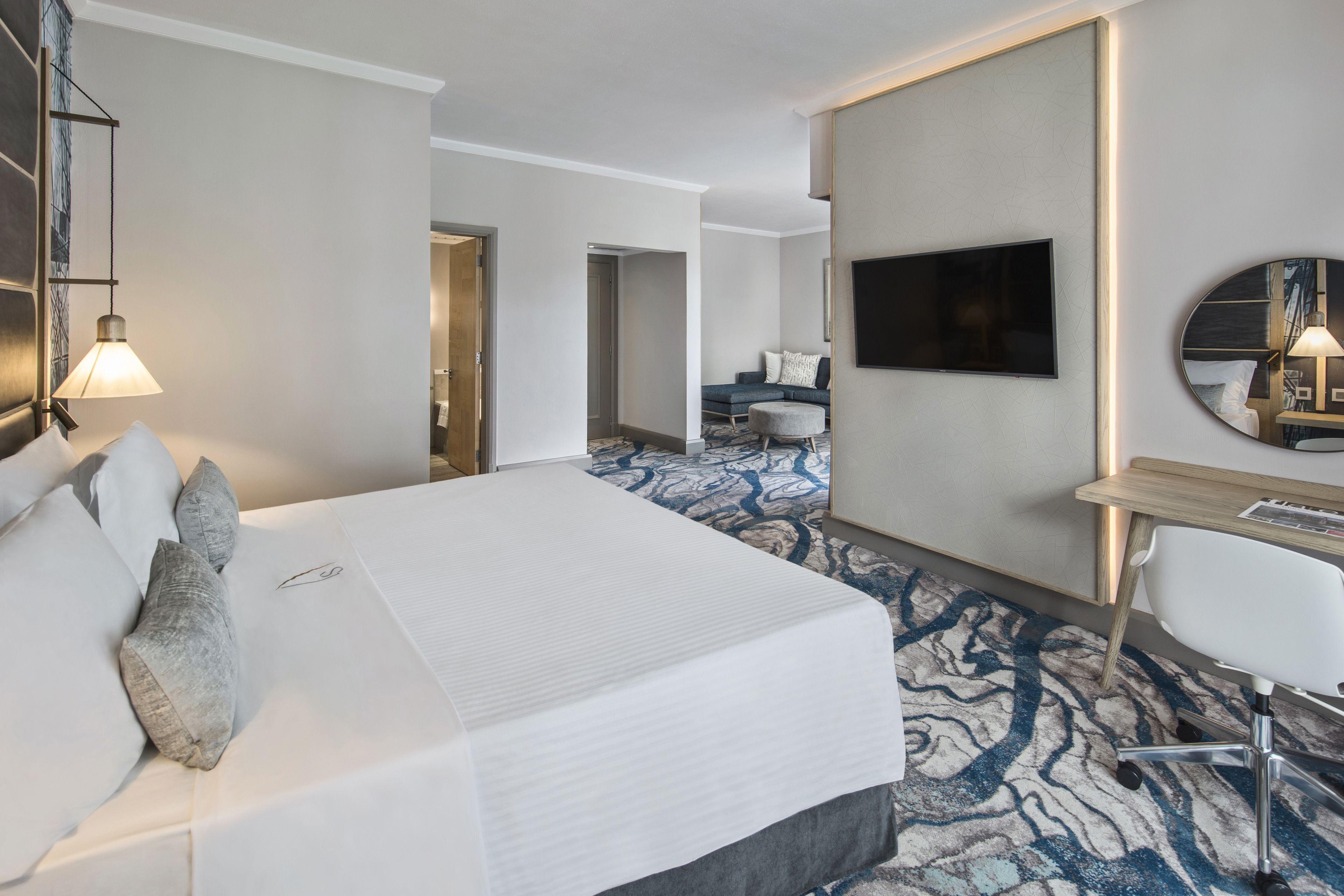 A hotel room with a large bed, a desk, a TV, and a mirror.