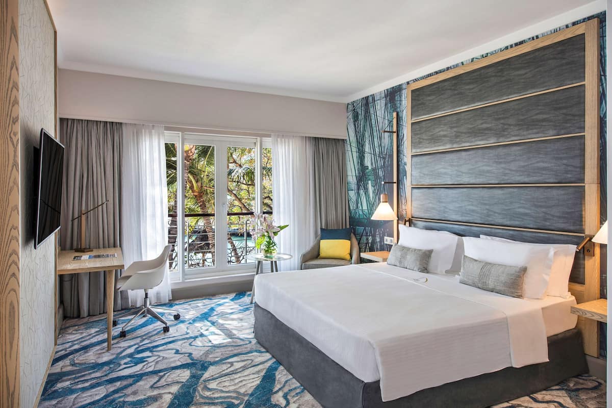 Habitación de hotel con una cama grande, un escritorio, una silla, un televisor y vistas al exterior.