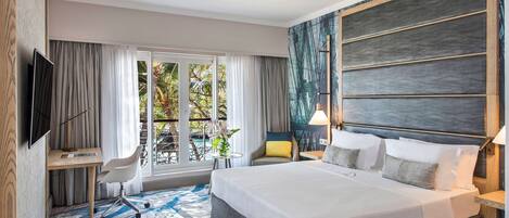 A hotel room with a large bed, a desk, a chair, a TV, and a view of the outdoors.