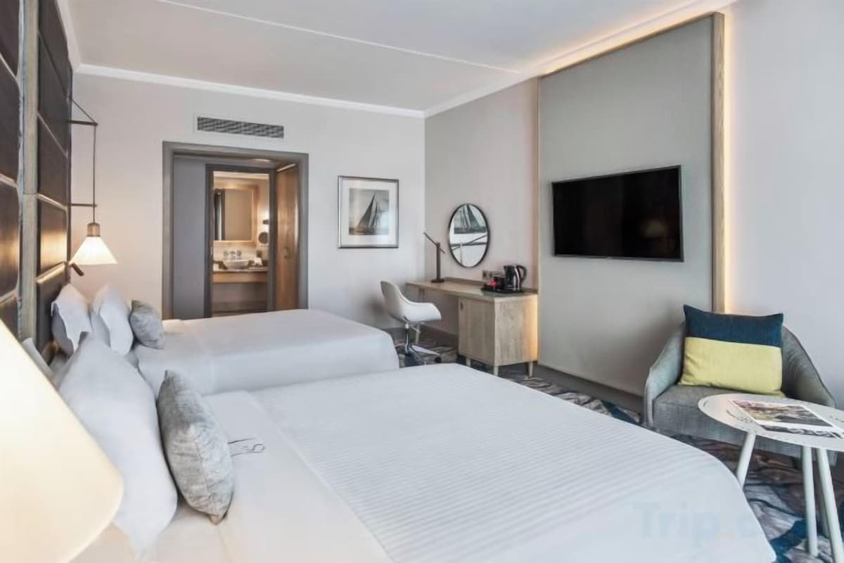 A hotel room with a large bed, a desk, a chair, a TV, and a small table.