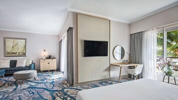 Habitación de hotel con cama, escritorio, televisor, sofá y un amplio ventanal con cortinas.