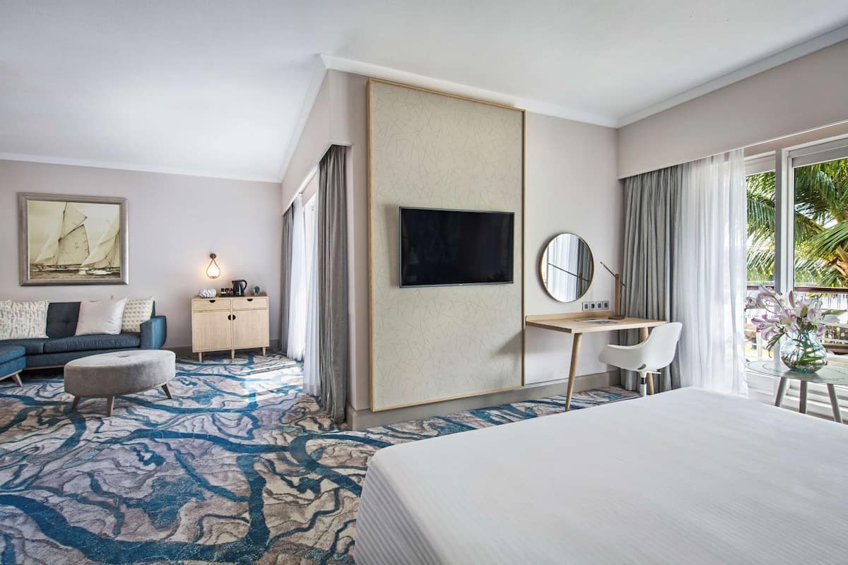 Una habitación de hotel con cama, escritorio, televisor, sofá, armario y una ventana grande.