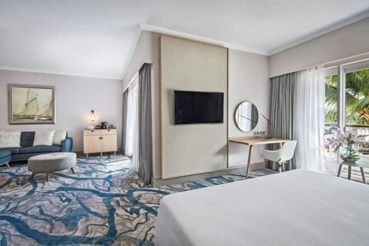 Habitación de hotel con cama, escritorio, televisor, sofá, armario y ventana grande con cortinas.