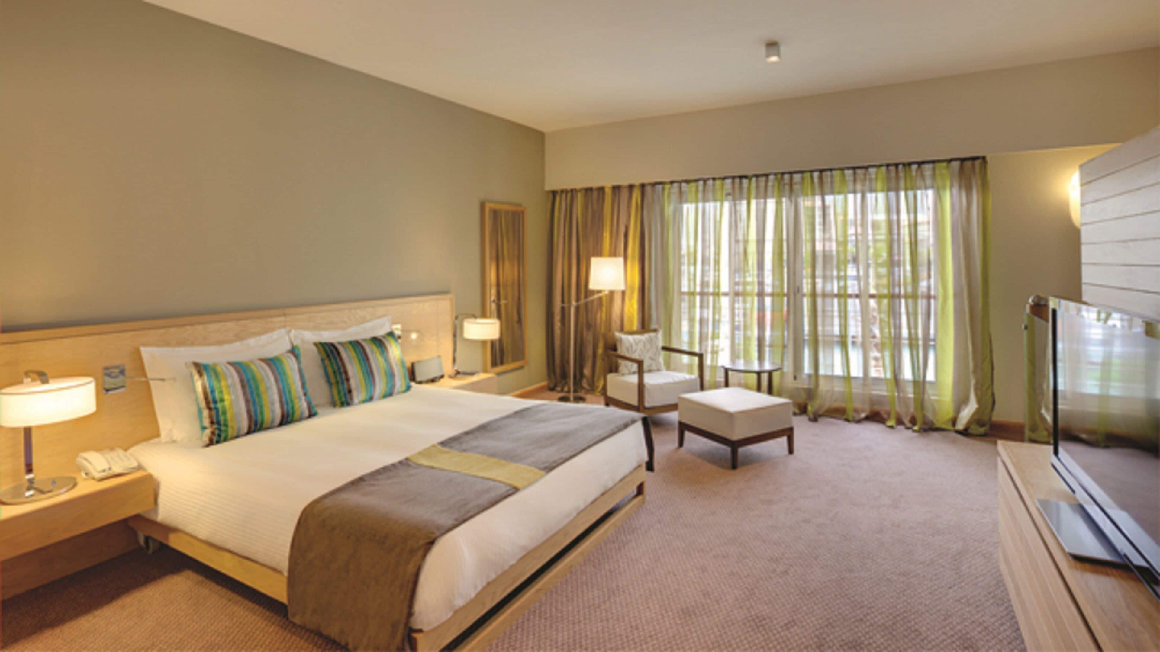 A hotel room with a large bed, a desk, a chair, a TV, and a window with curtains.
