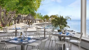 A seaside restaurant with outdoor seating, tables set with blue glassware, and a view of the ocean. - Le Suffren Hotel & Marina (Port Louis)