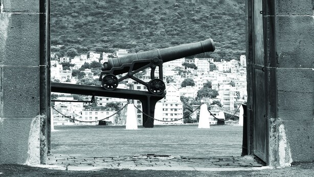A historical cannon through an arched stone doorway with a plaque reading "W.R." - Le Suffren Hotel & Marina (Port Louis)
