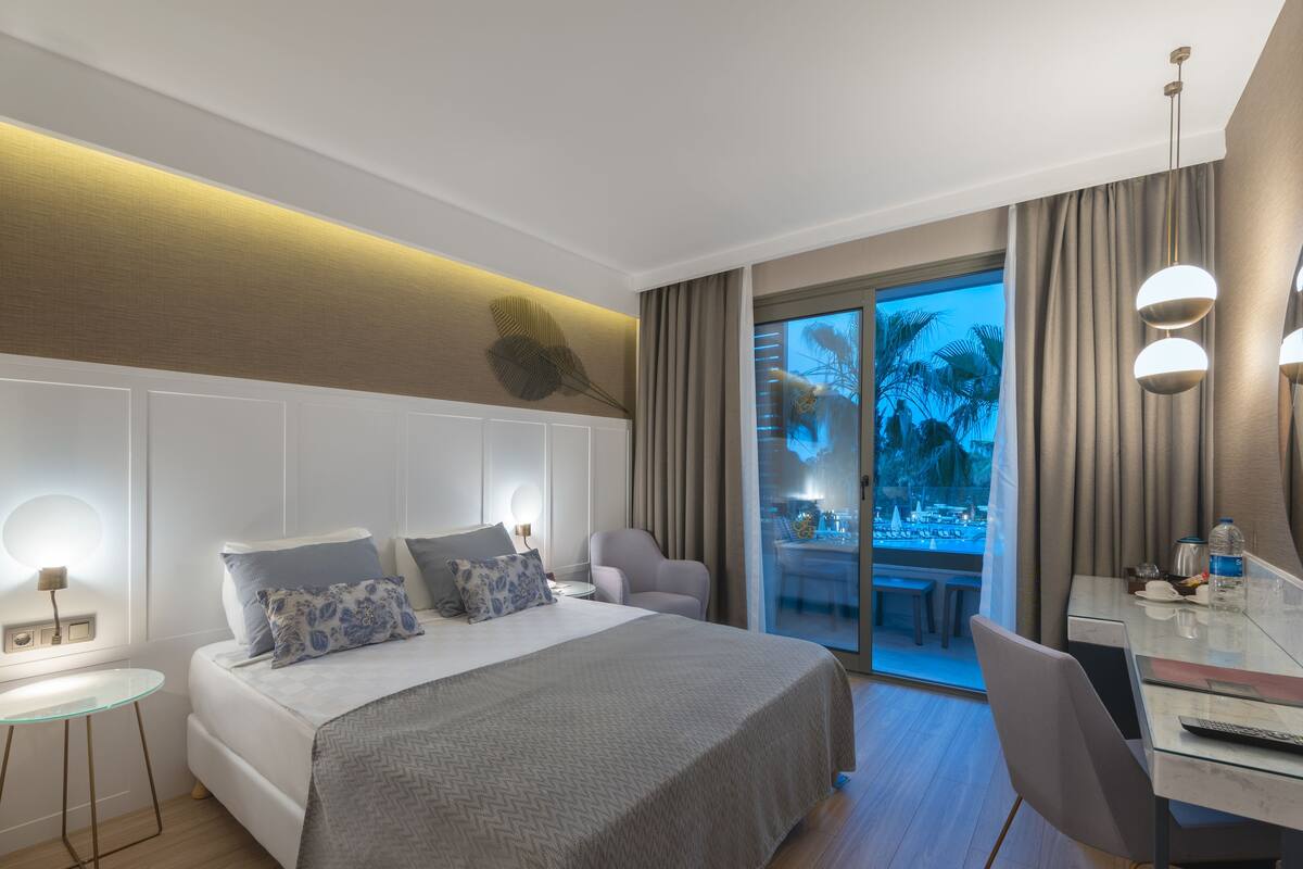 A modern hotel room with a large bed, a desk with a computer, and a TV.