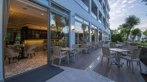 Un espace extérieur aménagé avec des tables et des chaises, une terrasse en bois et une entrée vitrée menant au bâtiment.