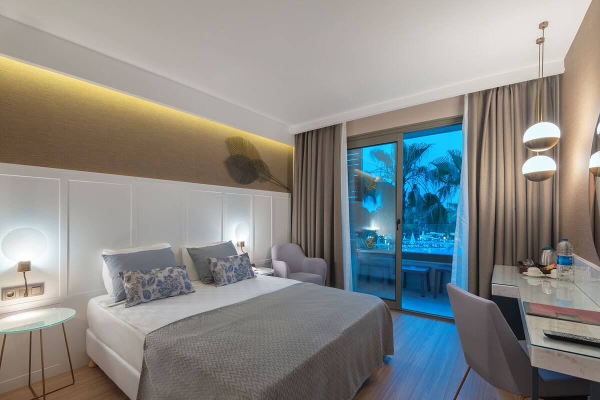 Ein modernes Hotelzimmer mit einem großen Bett, einem Schreibtisch mit Computer und einem Fernseher.