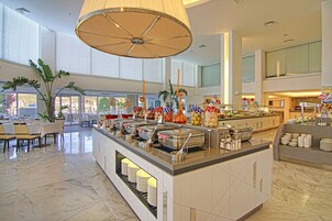 Un amplio hall de hotel con zona de buffet, disposición de asientos y ventanas grandes.