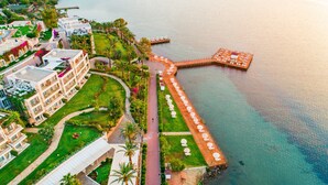 Vue aérienne d’un hôtel situé sur la côte, avec une longue jetée s’étendant dans l’eau, entouré d’une végétation luxuriante et d’une pelouse bien entretenue.
