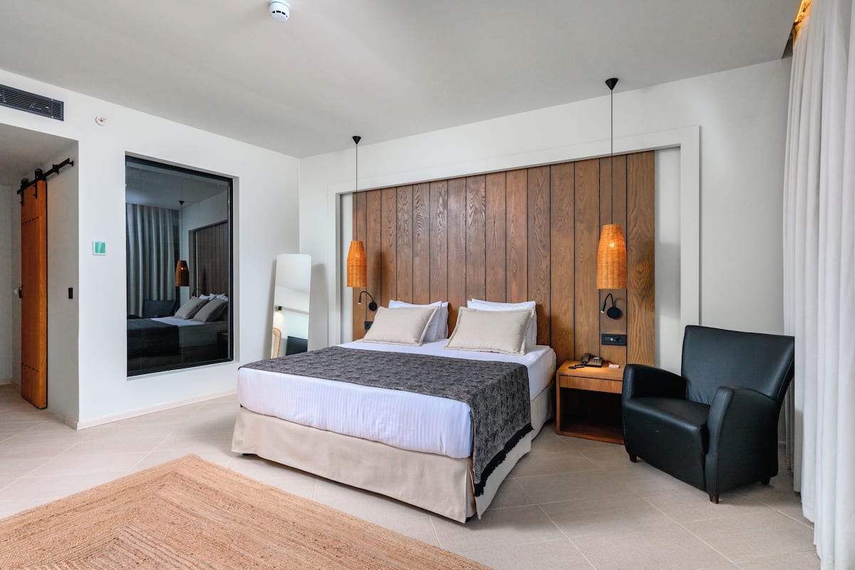 Een moderne slaapkamer met een groot bed, een houten hoofdbord, een zwarte stoel en een nachtkastje met een lamp.