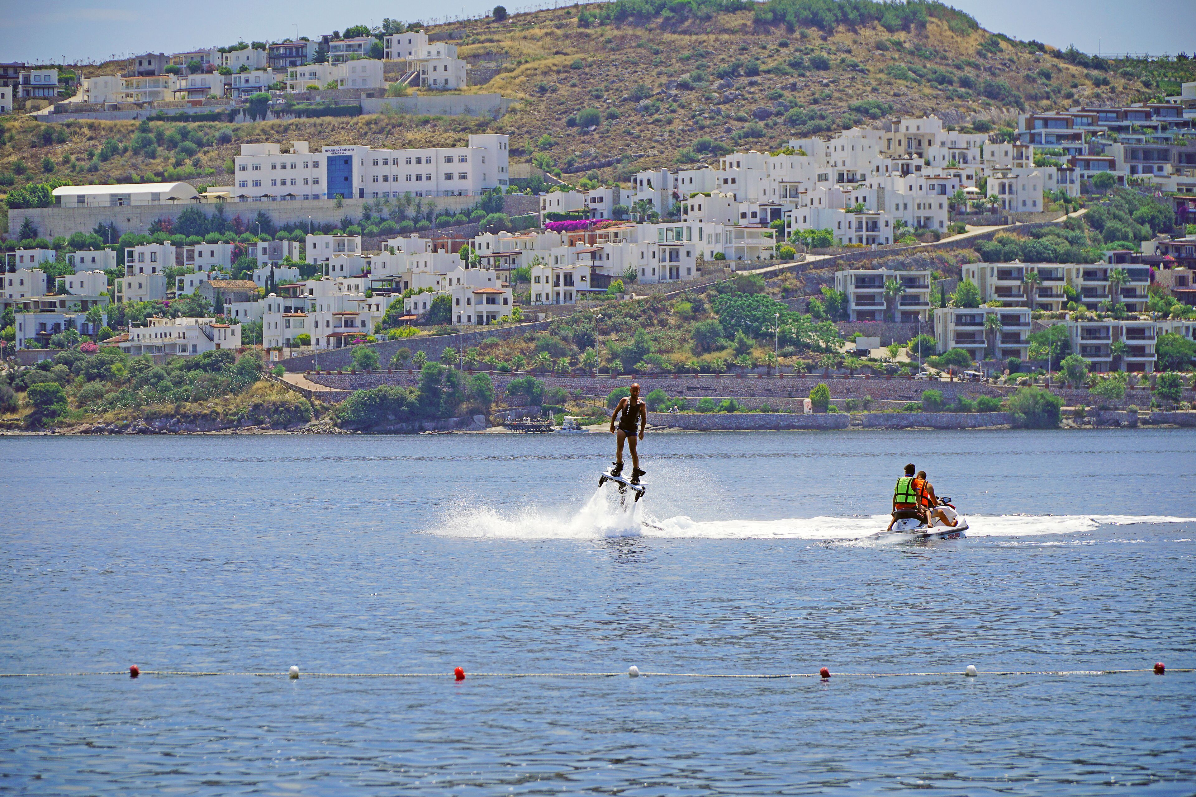 Zona costera con edificios, una persona practicando wakeboard y un jet ski.